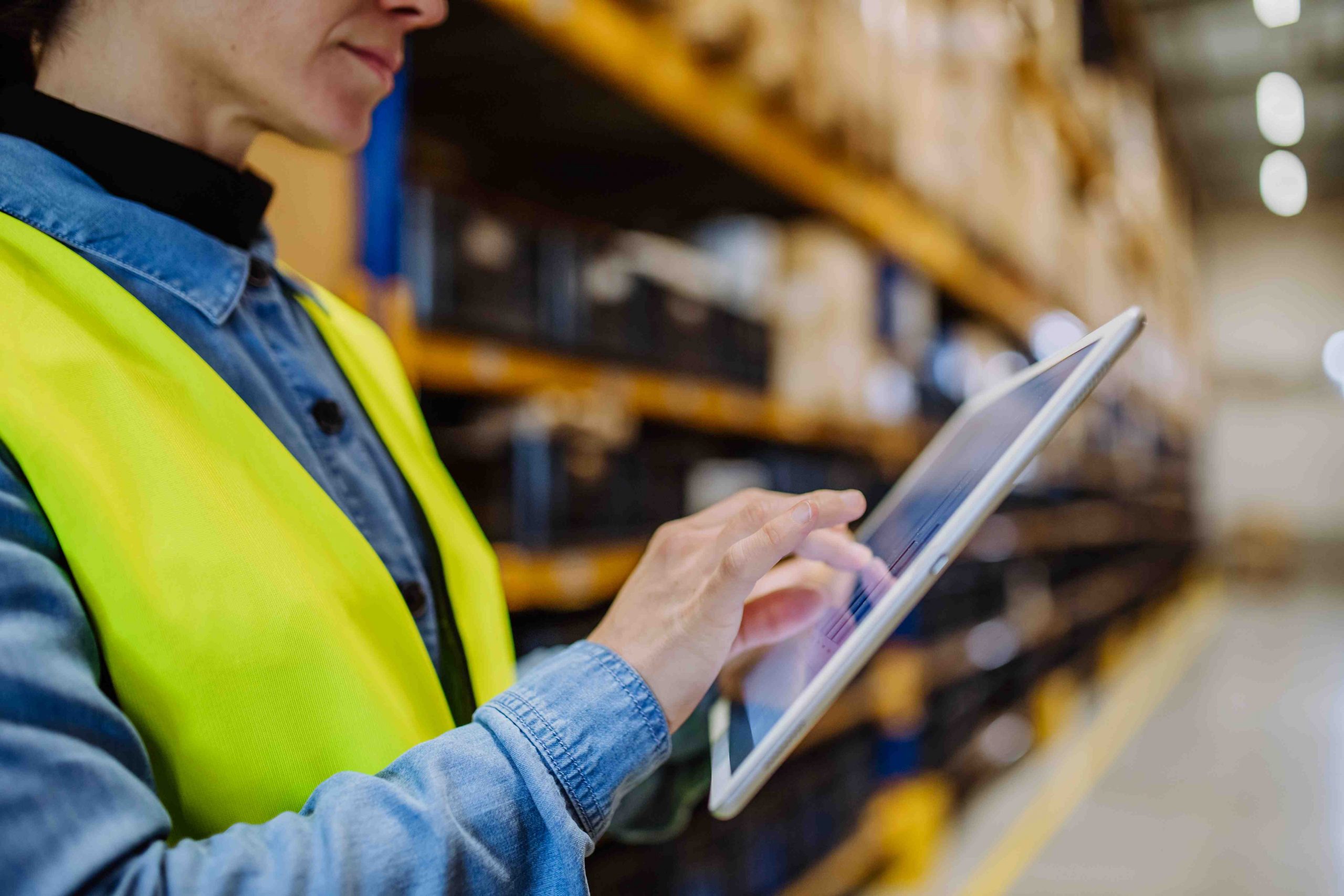 A female warehouse worker uses a WMS mobile solution on a tablet to manage inventory.